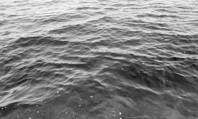 一张黑白照片，描绘了一些小波浪和气泡的水面.