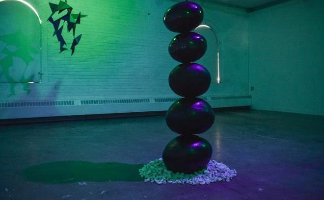 正面的黑色陶瓷球与绿色和紫色照明. 后面是“寻找和平”，一个带有锯齿三角形的钢结构建筑.  